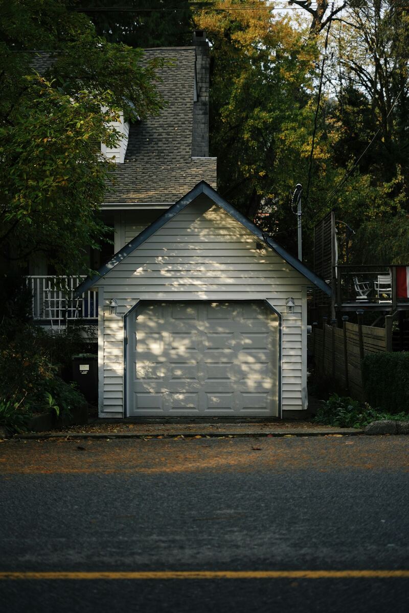 Detached single-car garage with white raised-panel door in dappled late-day light