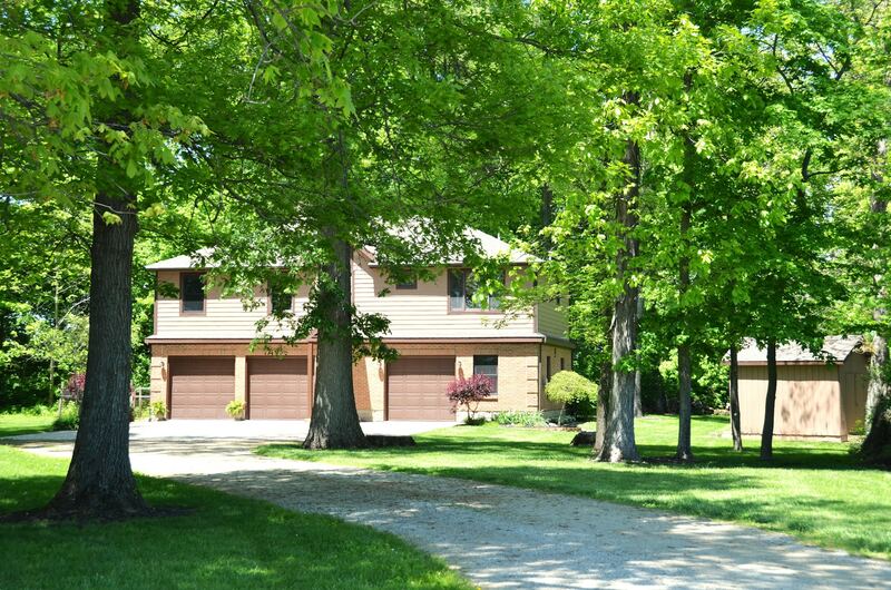 Two-story home with three brown garage doors and a gravel driveway under shade trees