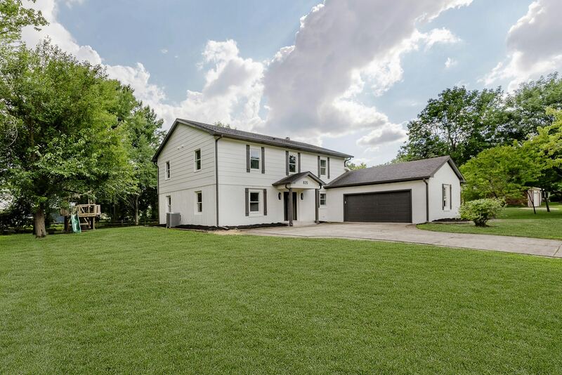 White two-story colonial-style home with a dark attached two-car garage door and lawn