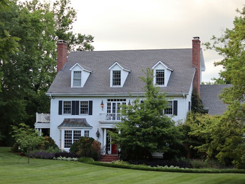 White colonial home with three dormers, black shutters, brick chimneys and landscaped lawn